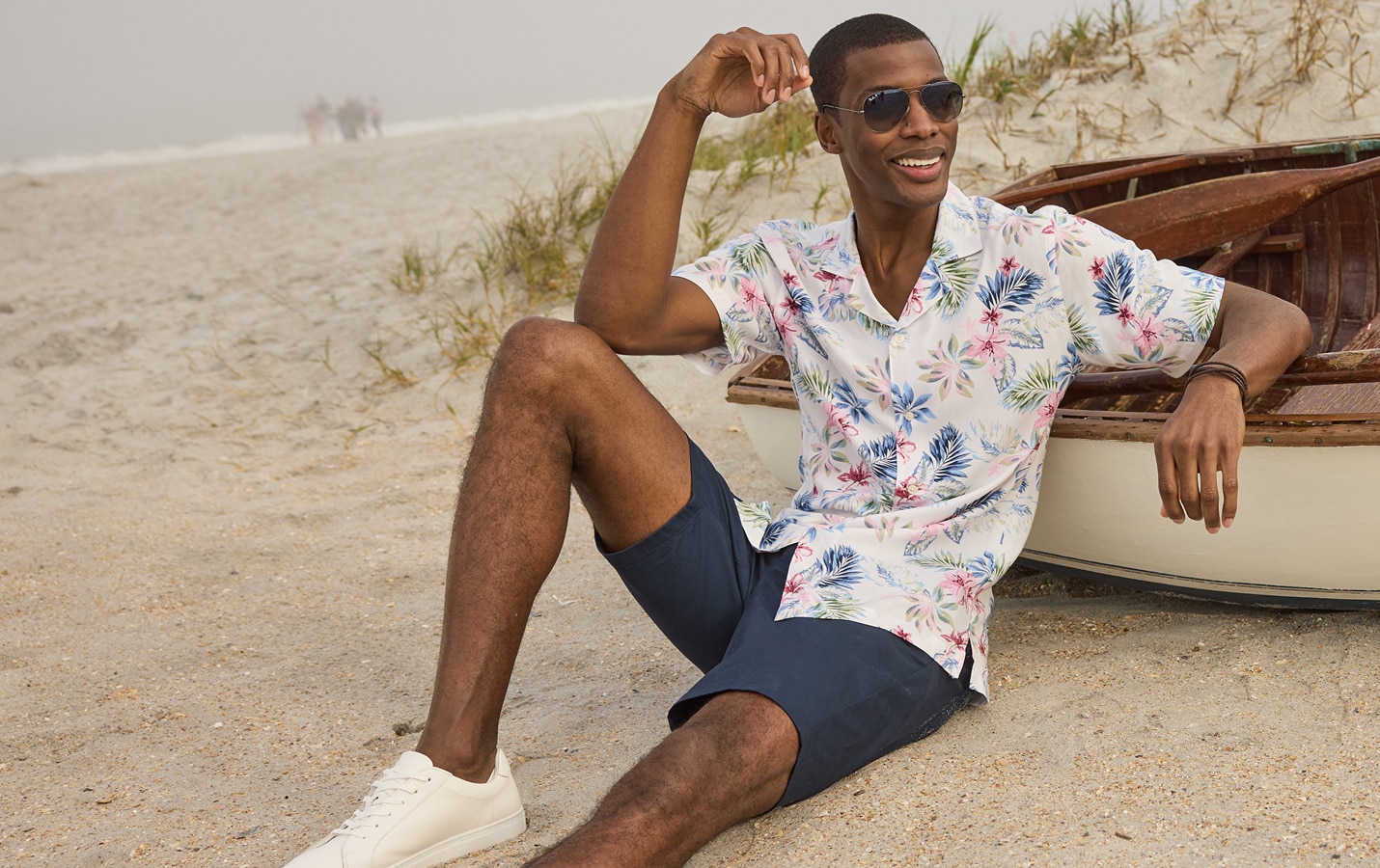 Man on a beach wearing a floral short-sleeve shirt and navy shorts