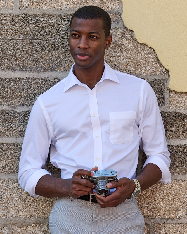 Man in a white dress shirt and grey plaid trousers holding a camera