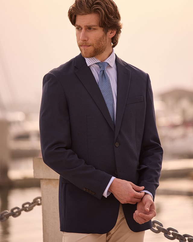 Man in a navy blazer, striped dress shirt, and tan trousers