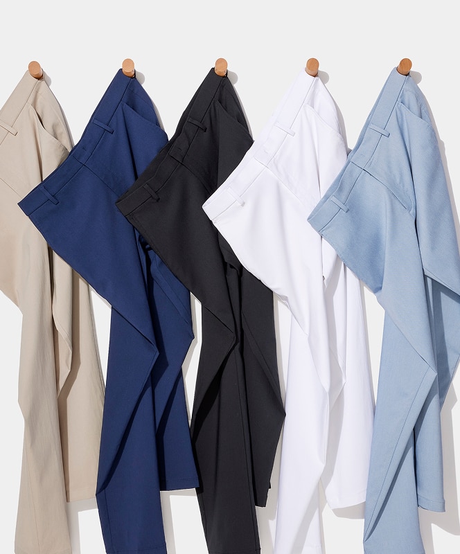 Five pairs of mens dress pants in beige, navy, black, white, and light blue hanging on wooden pegs