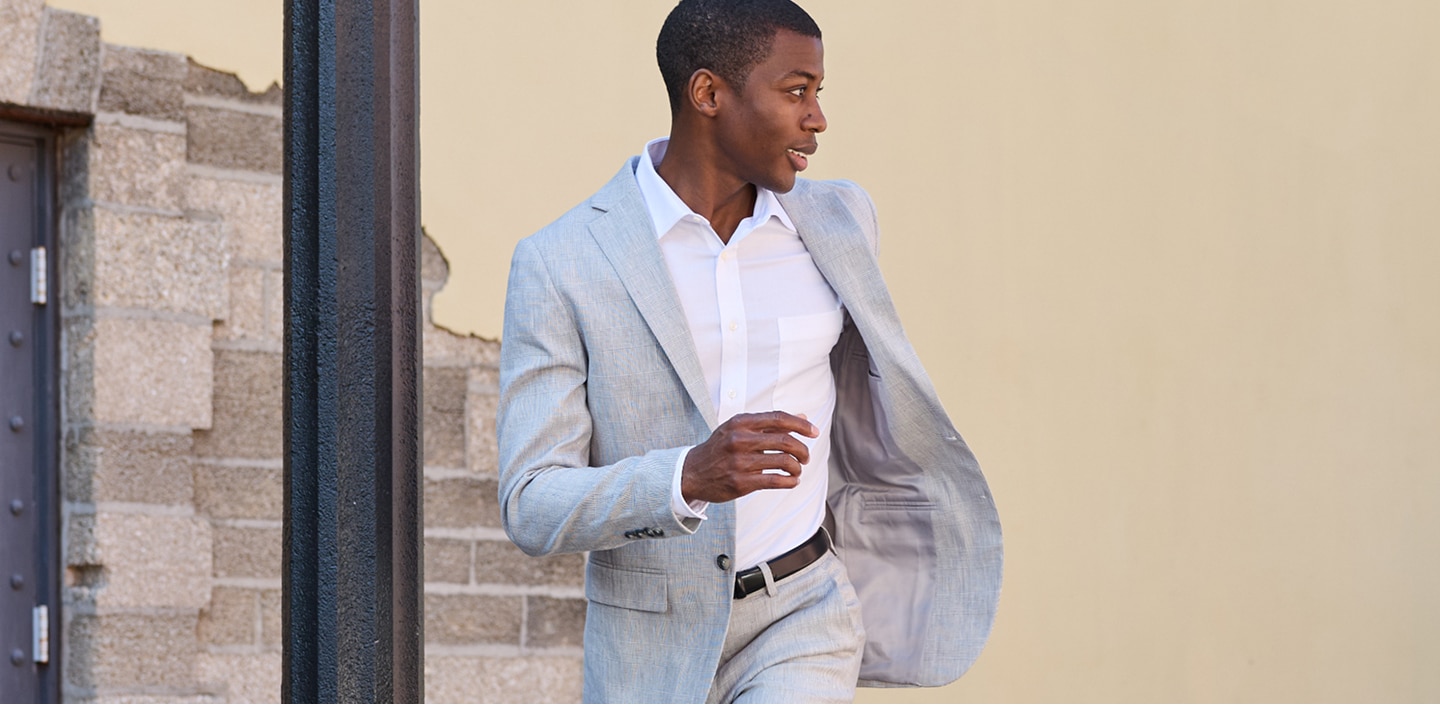 Man wearing a light grey plaid suit and white dress shirt walking outdoors