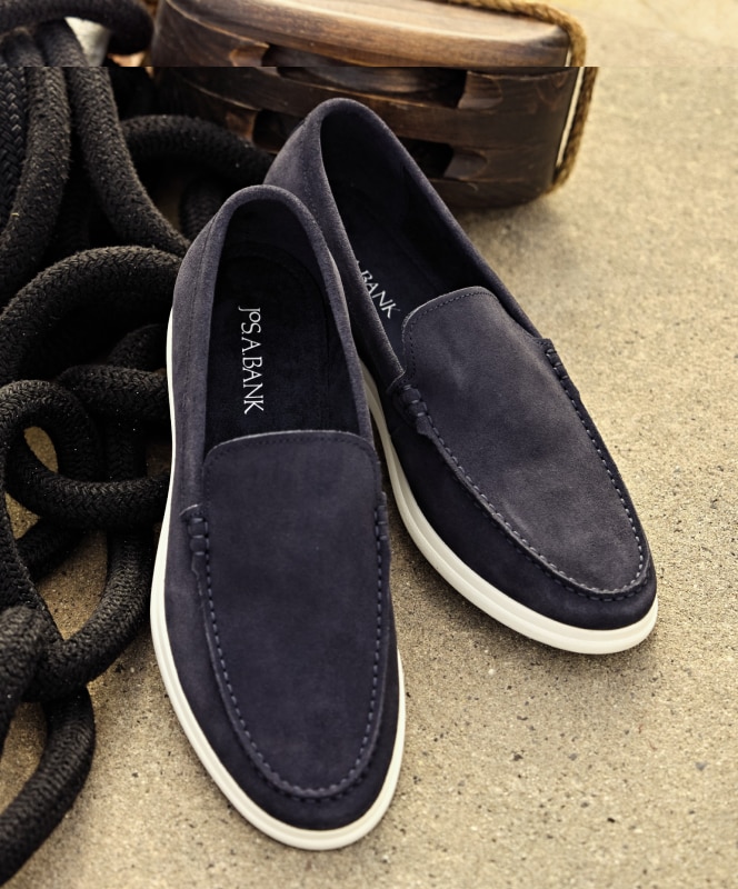 Jos. A. Bank navy blue suede loafers with white soles on a nautical background