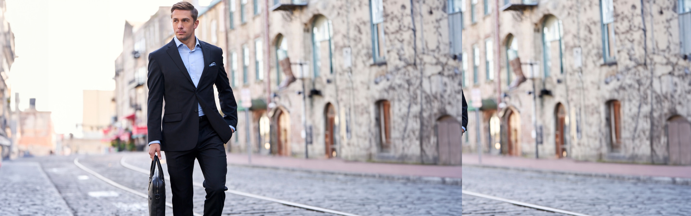 Man in a navy suit walking on a cobblestone street.