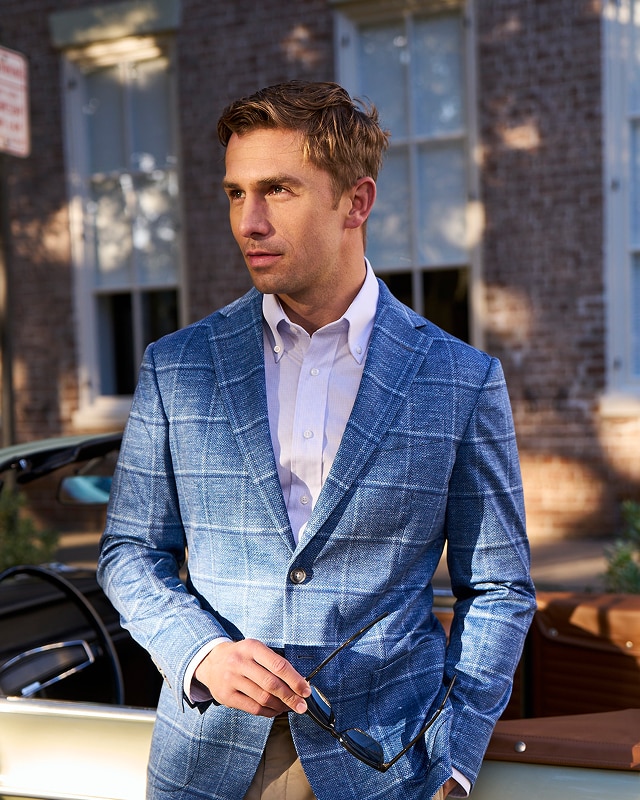 Man wearing a blue windowpane sportcoat and white dress shirt standing by a vintage car