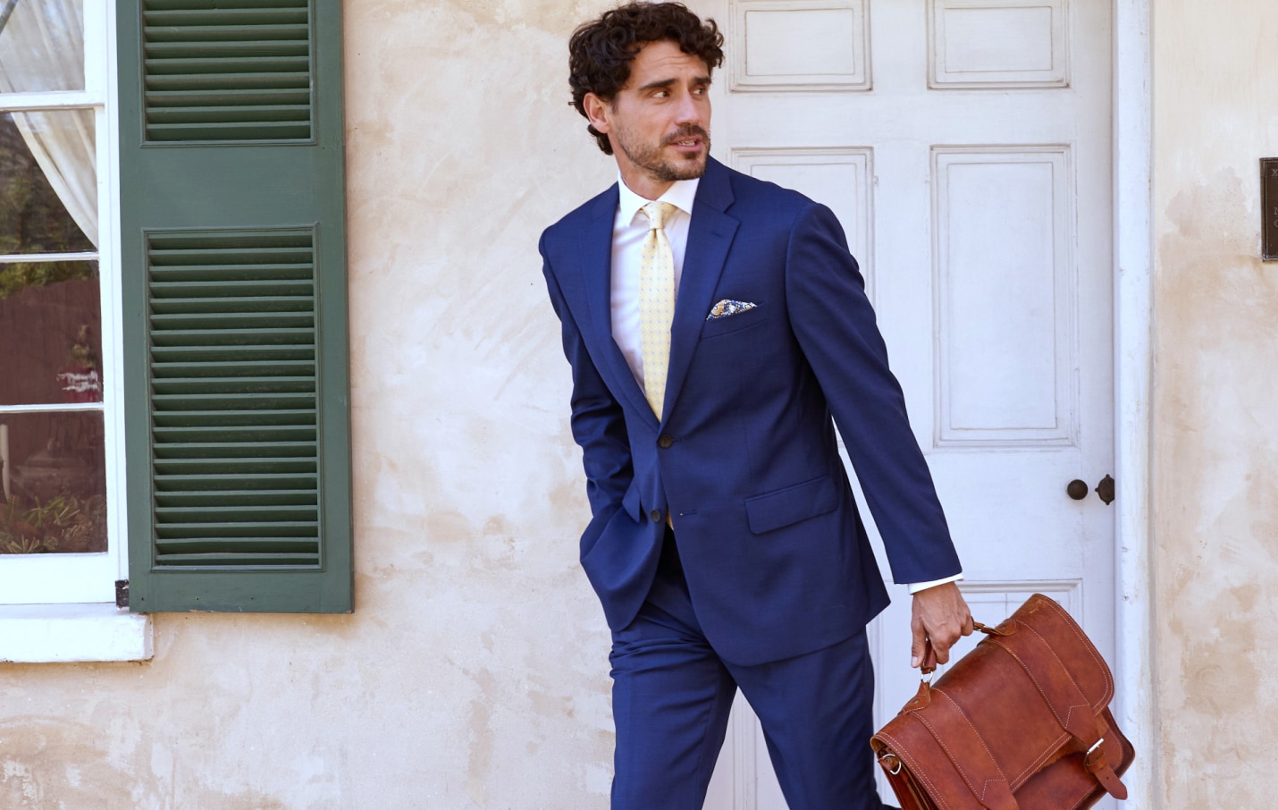 Man in a navy blue suit with a yellow patterned tie carrying a brown leather briefcase