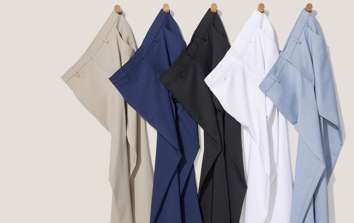 Pants in beige, navy, black, white, and light blue hanging on wall pegs