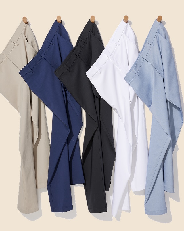 Five pairs of mens dress pants in beige, navy, black, white, and light blue hanging on wooden pegs