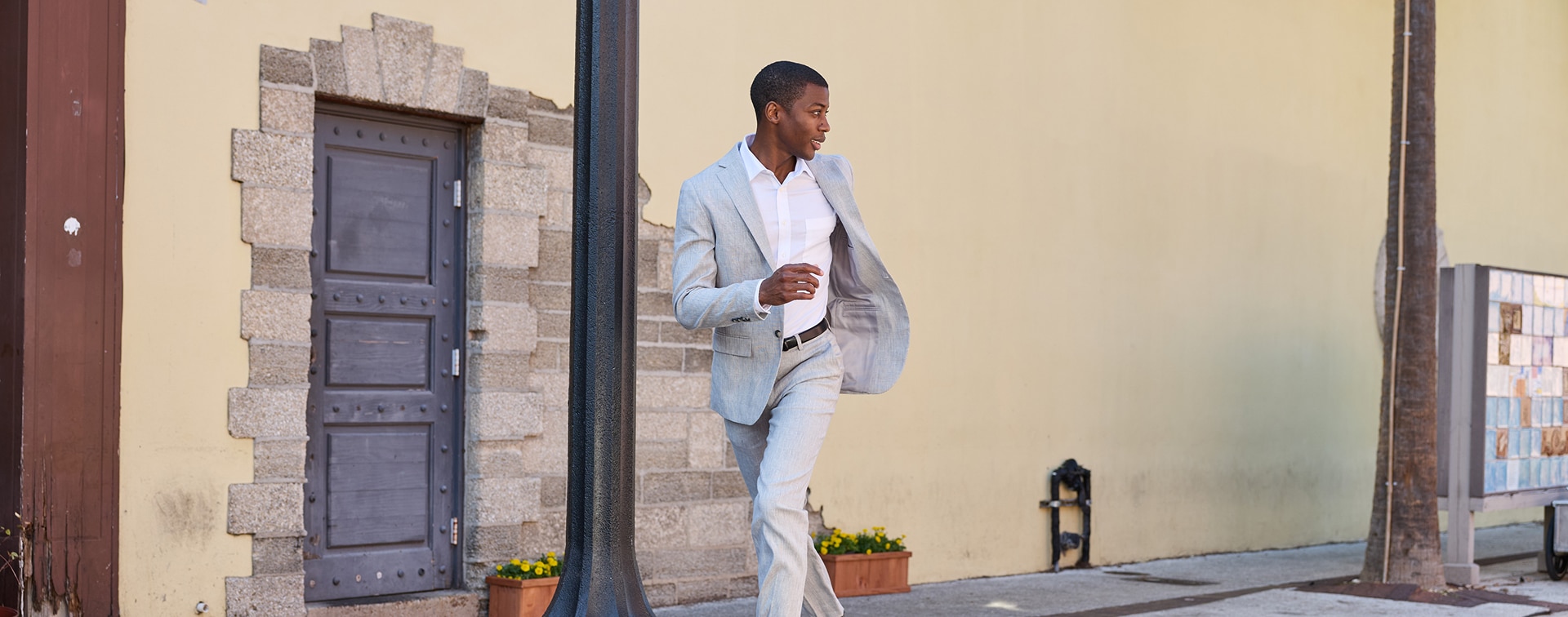 Man in a light grey suit and white dress shirt walking outdoors