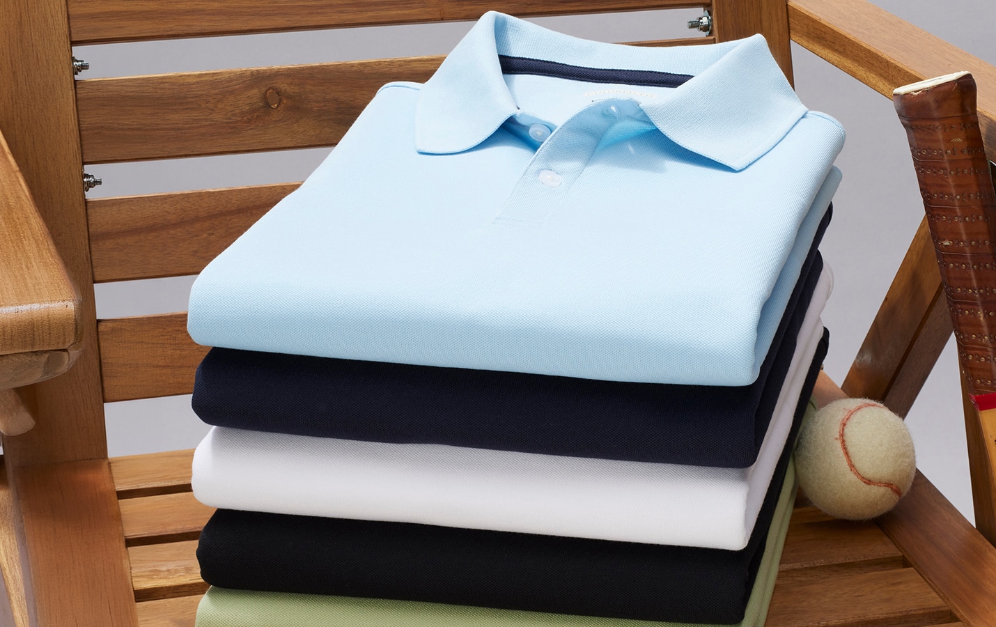 Stack of folded polo shirts in light blue, navy, white, black, and light green on a wooden chair