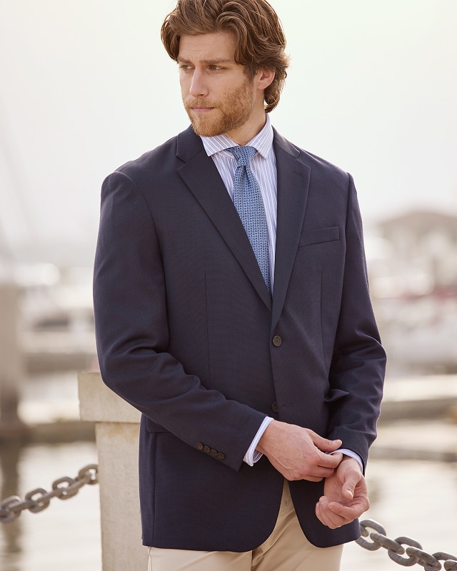 Man wearing a navy blazer, striped dress shirt, and tan trousers outdoors