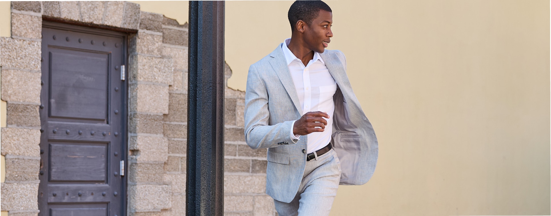 Man in a light grey suit and white dress shirt walking outdoors