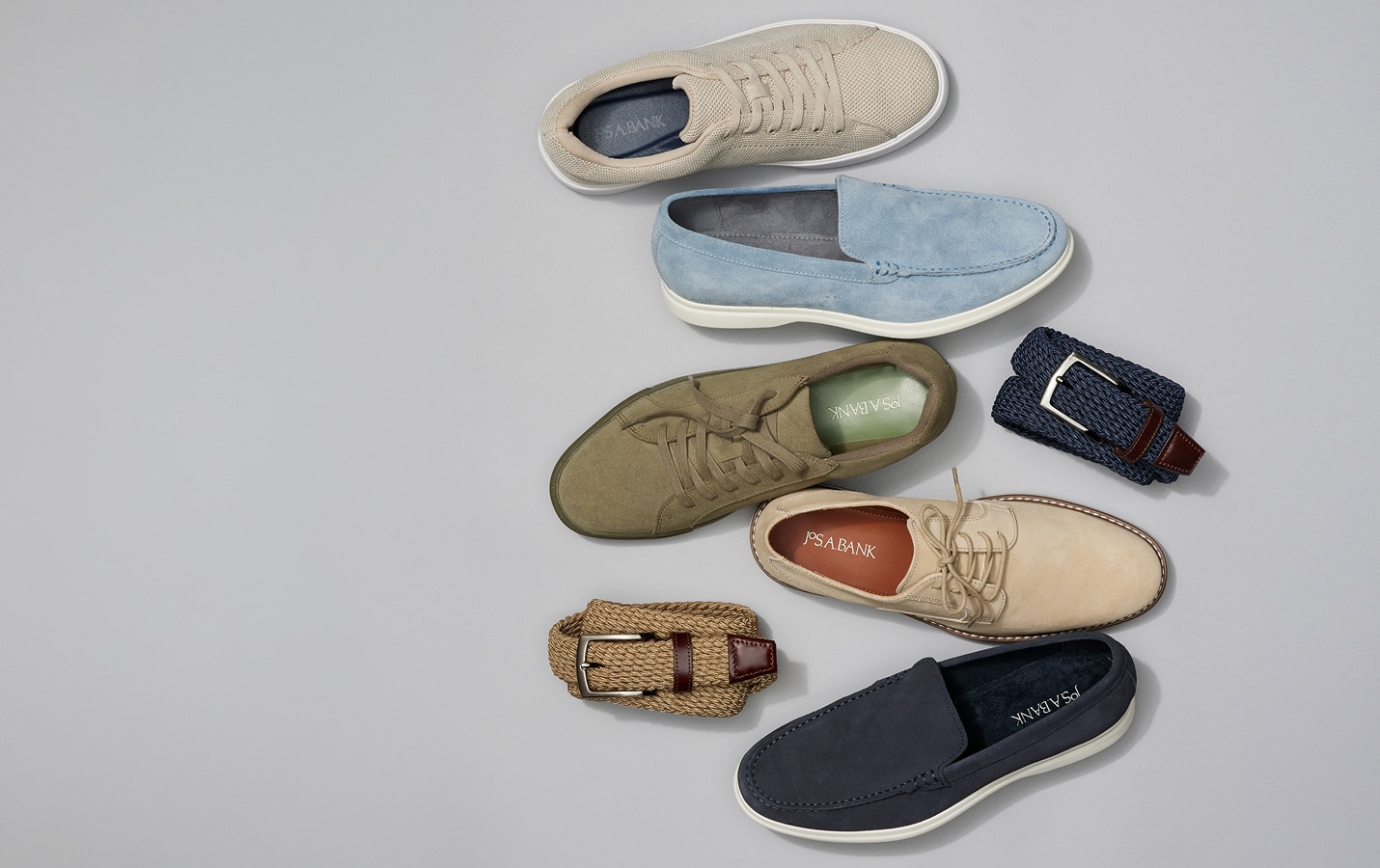 Assortment of mens shoes and woven belts on a grey background