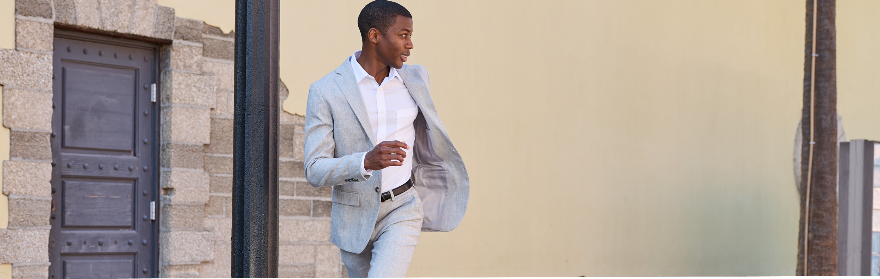 Man walking outdoors wearing a light grey linen suit and white dress shirt