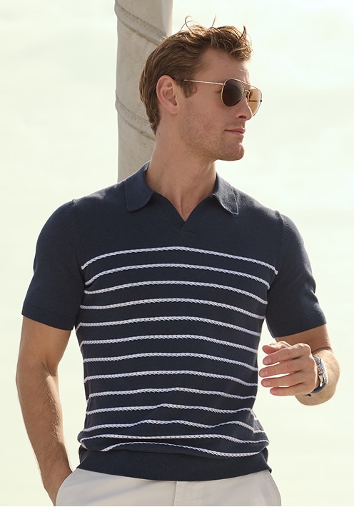 Man wearing a navy blue knit polo with white rope stripes and aviator sunglasses