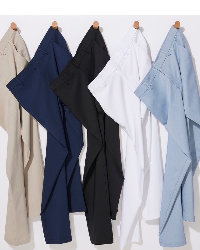Five pairs of pants in tan, navy, black, white, and blue hanging on pegs