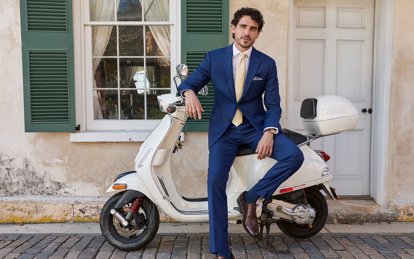 Man wearing a blue suit and yellow tie sitting on a white scooter
