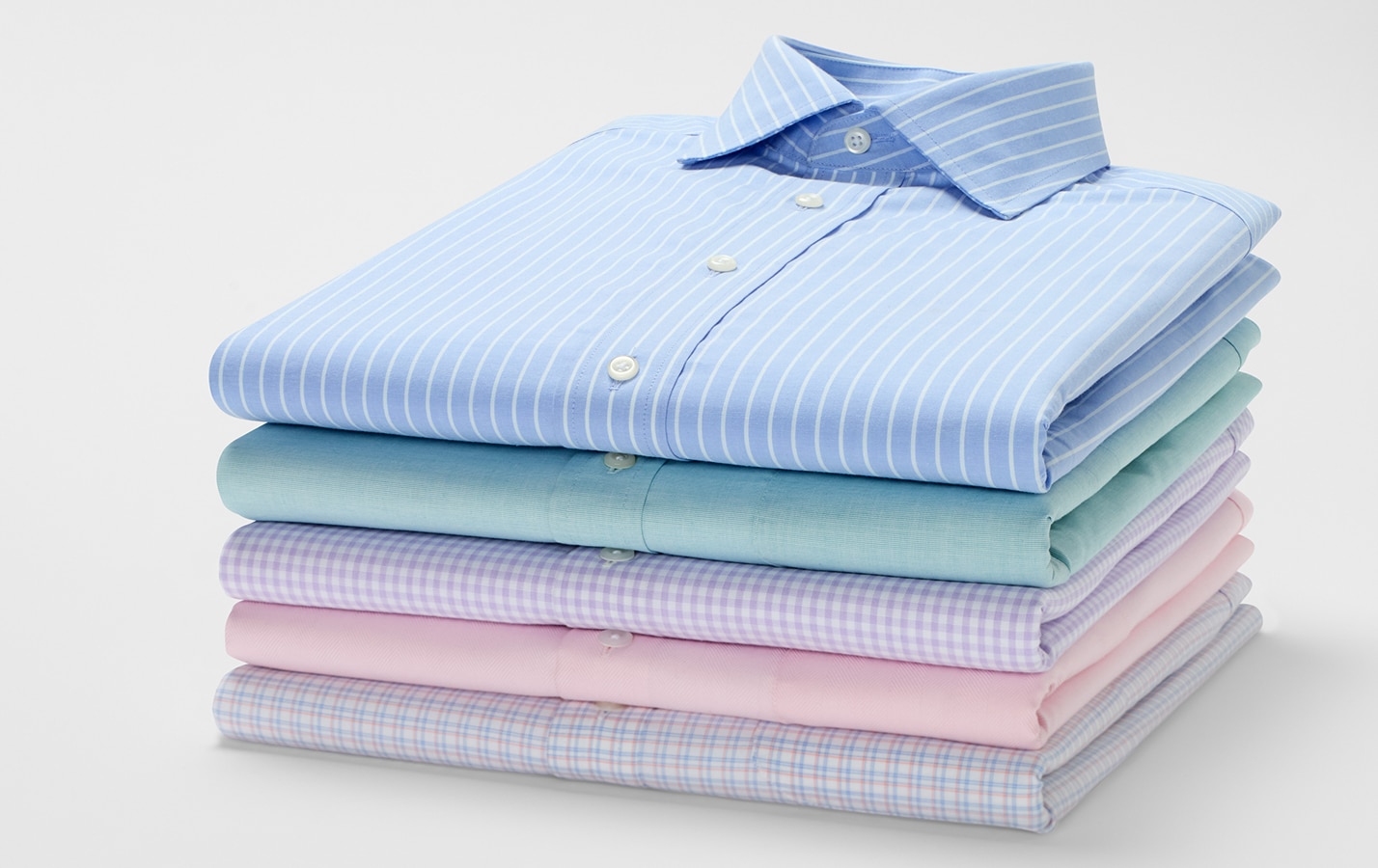 Stack of folded dress shirts in blue stripe, teal, gingham, pink, and plaid