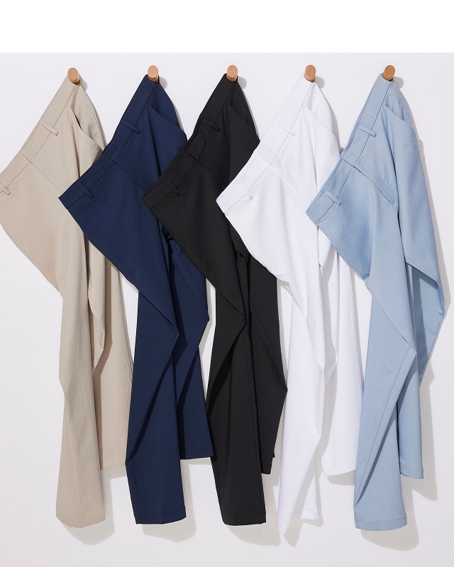 Five pairs of mens dress pants in beige, navy, black, white, and light blue hanging on wooden pegs