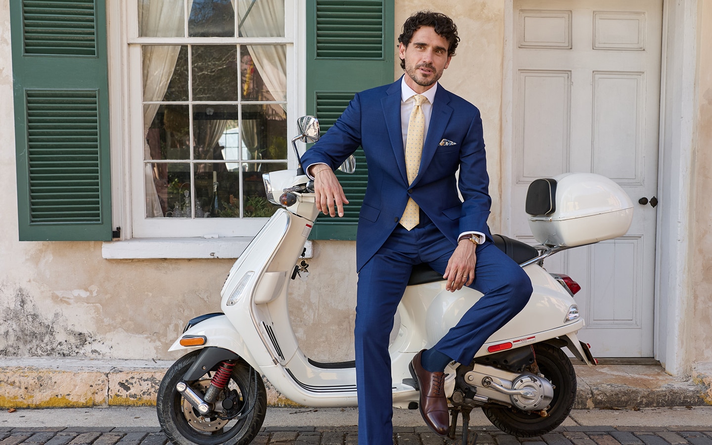 Man in a blue suit and yellow tie sitting on a white scooter