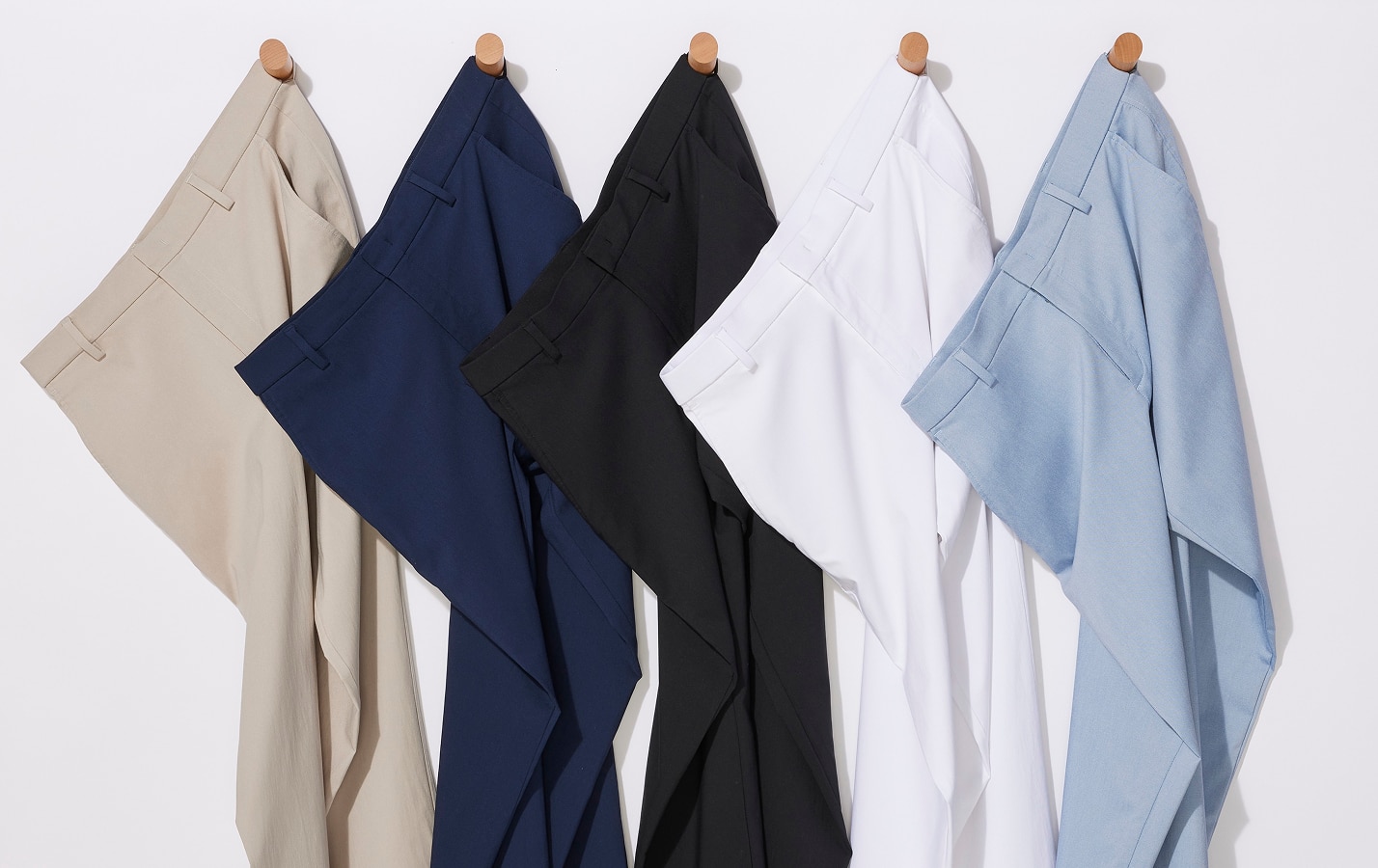 Five pairs of pants hanging on wooden pegs against a white wall