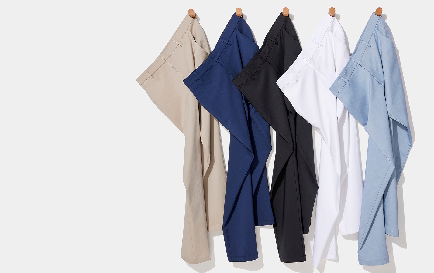 Five pairs of pants hanging on wooden pegs against a light gray wall