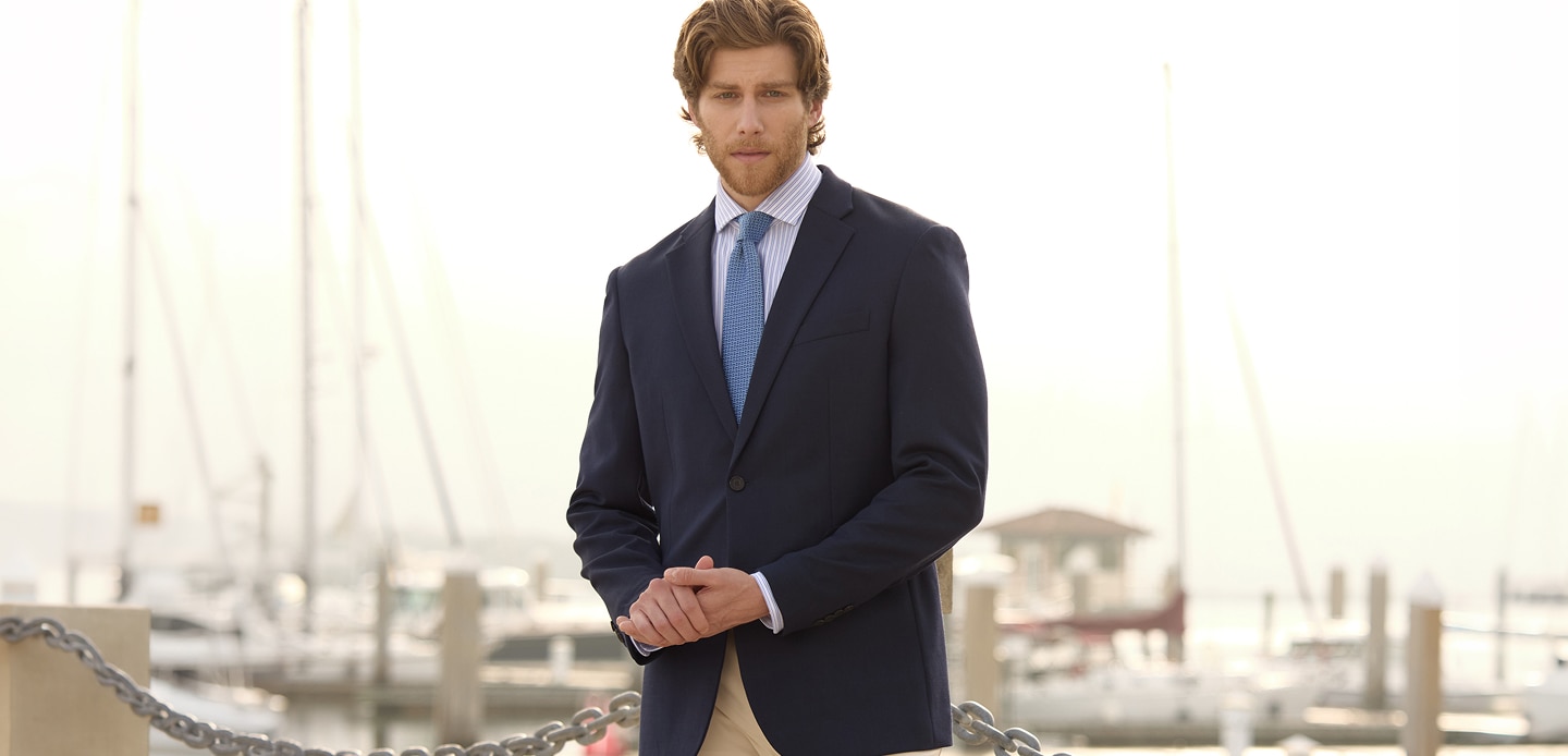 Man in a navy sportcoat, striped shirt, and blue tie standing at a marina