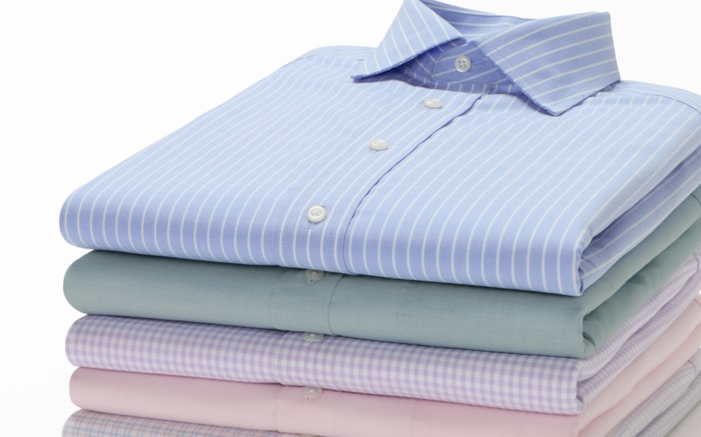 Stack of folded Traveler dress shirts in blue stripe, mint, lavender check, and pink