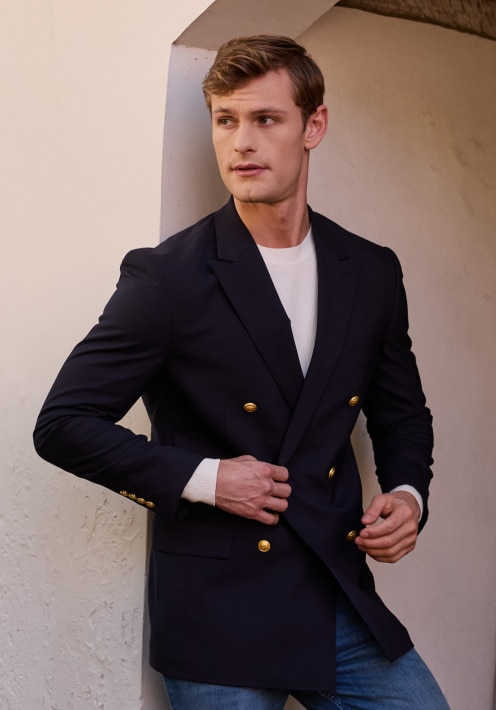 Man in a navy double-breasted blazer with gold buttons over a white sweater
