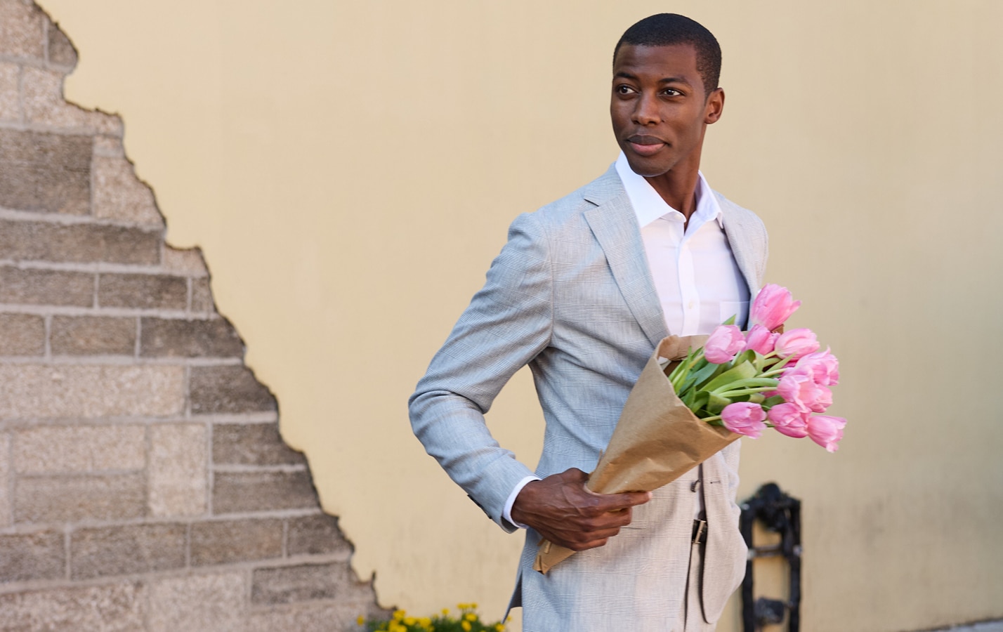 Man in a light grey suit holding a bouquet of pink tulips