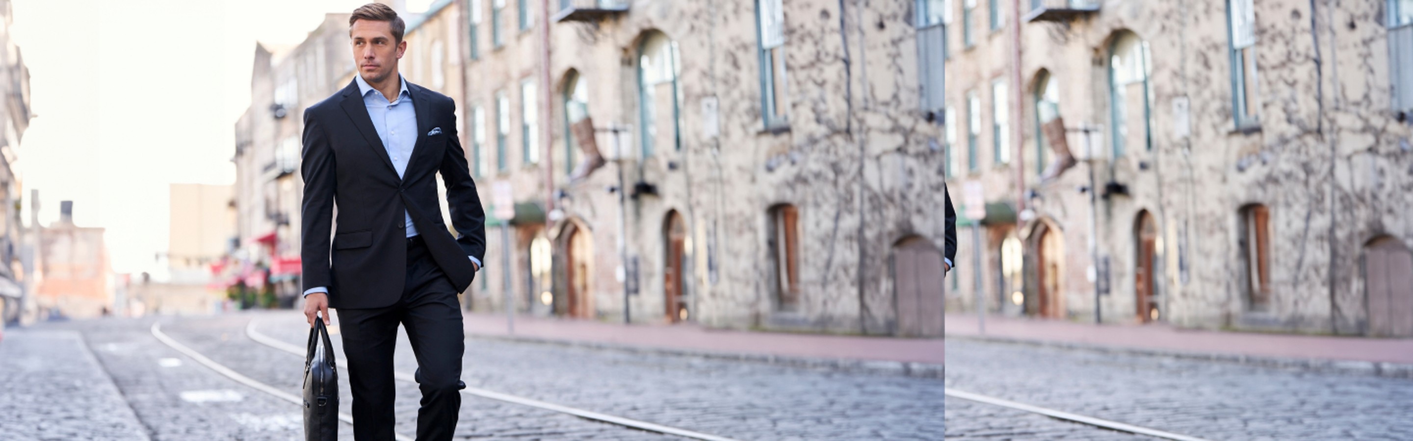Man in a navy suit carrying a briefcase while walking down a cobblestone street