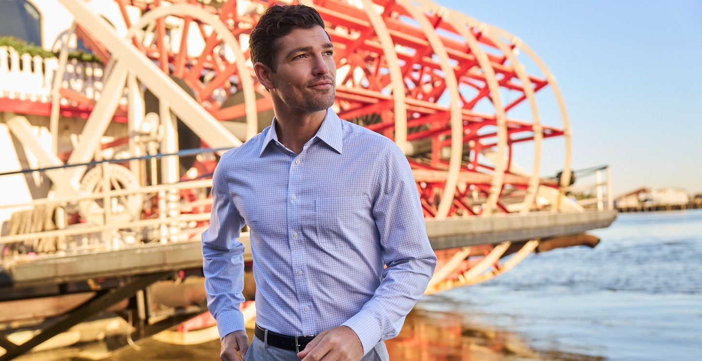 Man wearing a light blue checked dress shirt near a riverboat