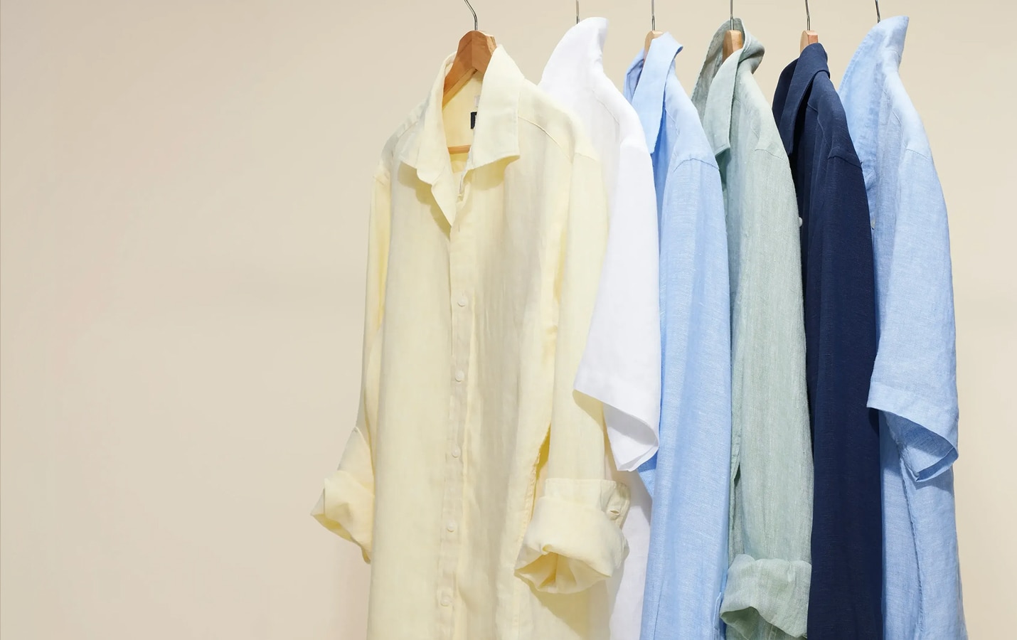 Casual linen shirts in yellow, white, light blue, sage, and navy hanging on a rack