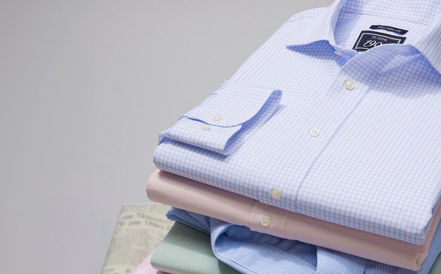 Stack of folded dress shirts in assorted colors and patterns with a tie