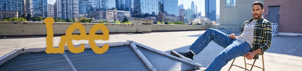 Lee brand banner featuring a man in a plaid flannel shirt and blue jeans sitting on a city rooftop with a skyscraper skyline background