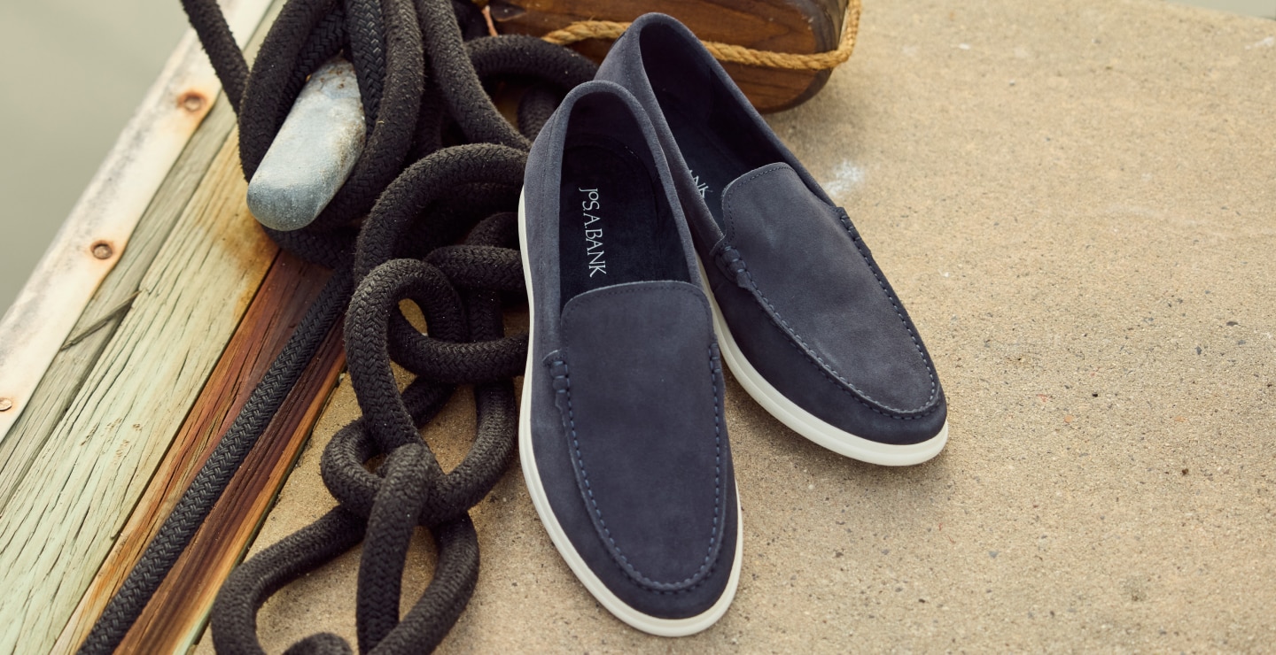 Navy suede loafers on a sandy surface.